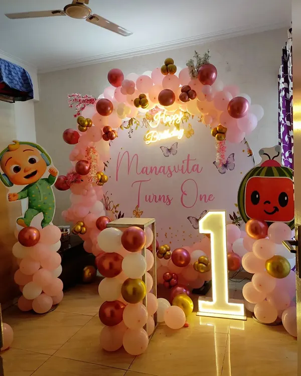 A Cocomelon theme is a favorite for first birthdays. Here, I created a full party backdrop for 'Manasvita Turns One' with character cut-outs, a pink and rose gold balloon arch, and a large light-up number '1'.