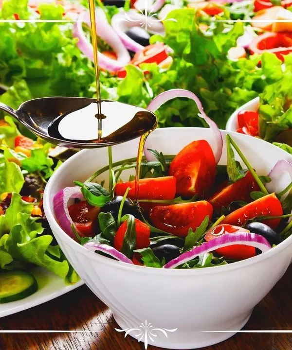 A fresh and vibrant salad featuring mixed greens, cherry tomatoes, and red onions, being dressed with extra virgin olive oil. We believe in using simple, high-quality ingredients to create delicious and healthy salad options.