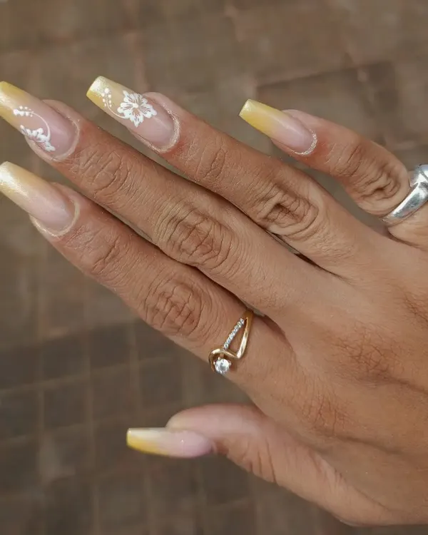 A beautiful set of long, square-shaped nails with a yellow ombre base and delicate, hand-painted white floral details.