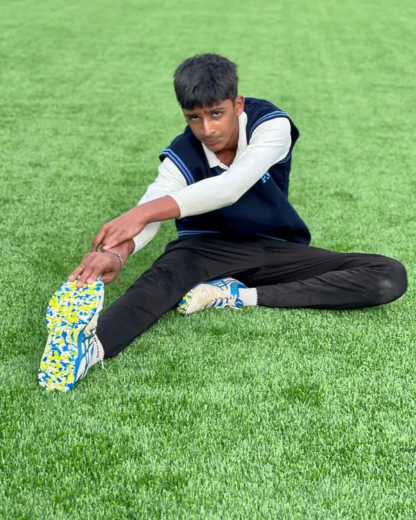 A young player performs a hamstring stretch on the lush astroturf. Flexibility is a key component of our fitness routine, helping with injury prevention and agility on the field.