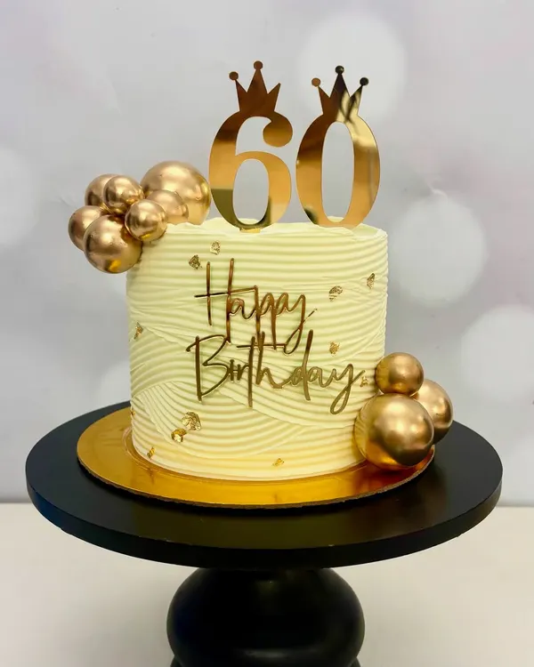 Celebrating 60 years in style! This elegant birthday cake features a beautiful wave texture, gold spheres, and a custom gold '60' topper with crowns. It’s designed to be a memorable centerpiece.