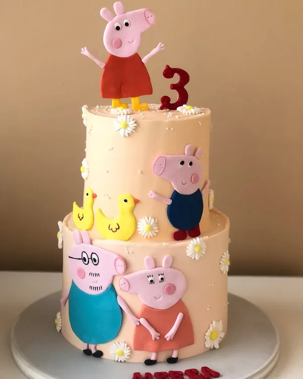 A cheerful two-tiered cake for a Peppa Pig fan. This design features the whole family, handcrafted and placed on a lovely pastel cake with little flowers.