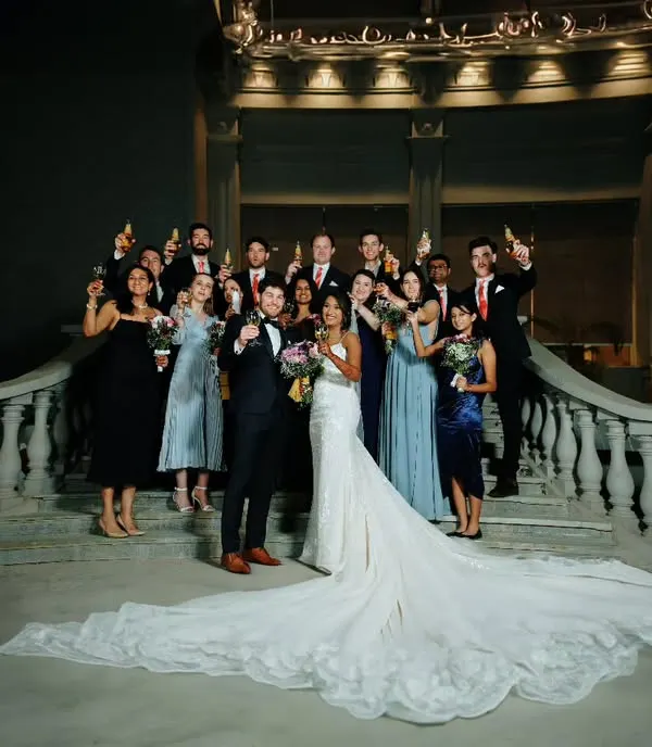 A beautiful group portrait from a cross-cultural wedding, with the bride in a stunning white gown with a long train, surrounded by her happy guests.