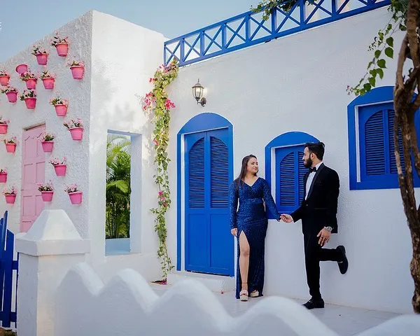 Yash and Priyanshi pose against a beautiful white building with vibrant blue doors, reminiscent of a Greek island. This set is perfect for couples wanting a clean, bright, and destination-style photoshoot.
