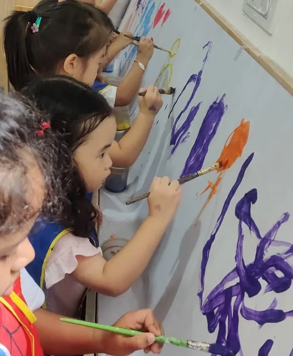 A group of young artists completely absorbed in creating a large-scale abstract mural. This collaborative painting activity encourages teamwork, communication, and shared creative expression.
