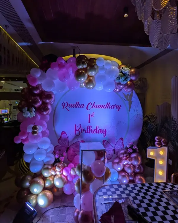 A magical butterfly-themed first birthday for Radha. The round backdrop is surrounded by a pink and rose gold balloon arch, with a large light-up number '1' to mark the special milestone.