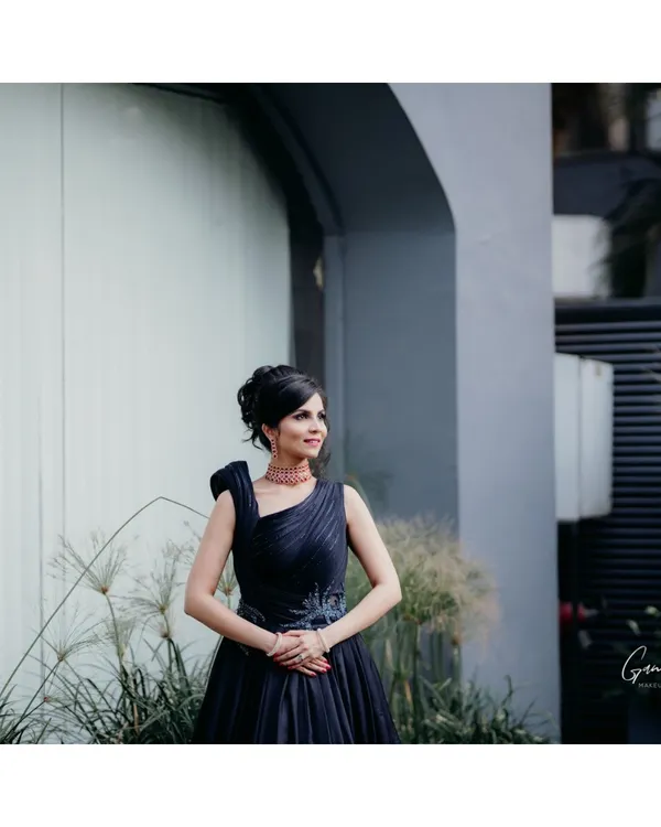 A full-length portrait showcasing a sophisticated cocktail look. The bride's elegant dark blue gown is paired with a chic updo and polished makeup, creating a look of modern grace and style.