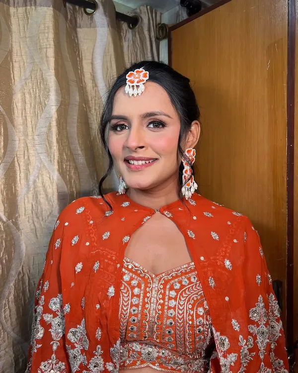 A flawless blend of beauty and grace in this vibrant orange outfit. The makeup features a soft smokey eye and glowing skin.