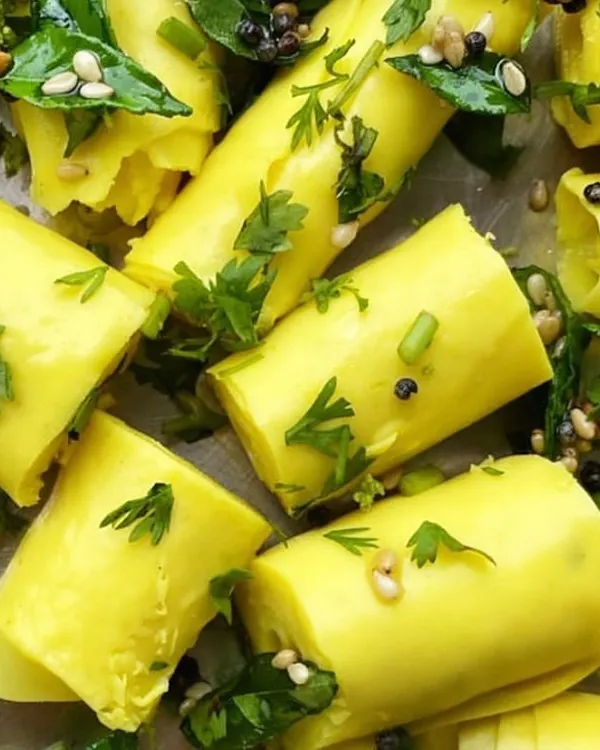 A close-up of our perfectly rolled Khandvi. You can see the delicate texture of the gram flour sheets, garnished with mustard seeds and fresh herbs. It's a light yet flavorful snack ideal for any time of day.