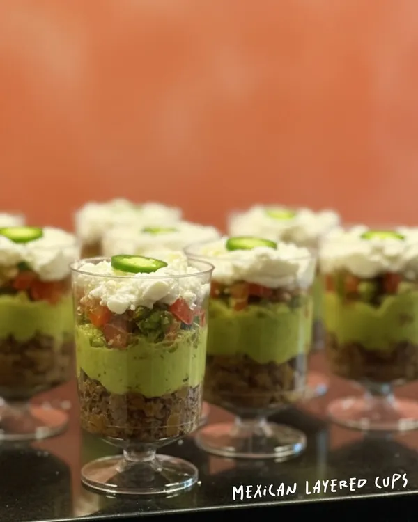 My Mexican Layered Cups are a flavor bomb. I layer savory beans, fresh guacamole, zesty salsa, and cool sour cream, topped with a slice of jalapeño for a little kick. They are a party in a cup.