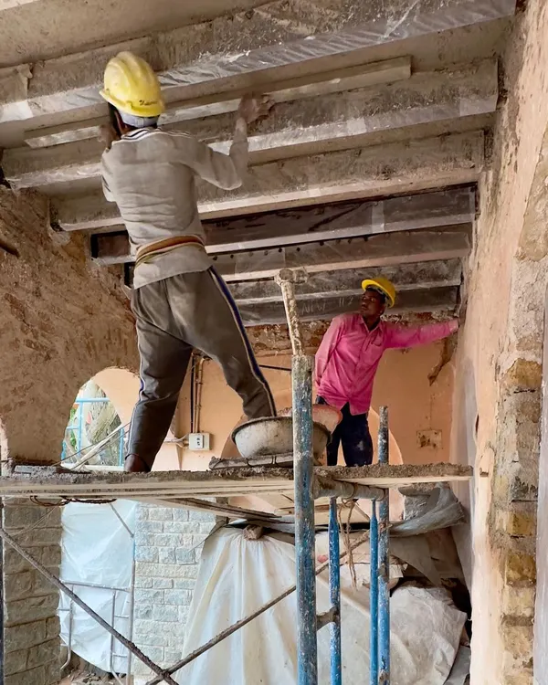 Two craftsmen work on restoring the timber ceiling beams of a historic school. This delicate process involves strengthening the original structure while preserving its aged character, a core principle of our conservation work.