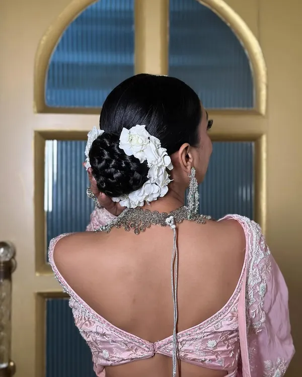 A detailed view of a bridal bun, intricately woven and adorned with fresh white flowers. This style is a perfect example of a classic yet modern updo for a wedding ceremony.