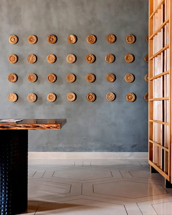 A detail from the Anthea Pharma project, showing the eye-catching hexagonal terrazzo flooring with brass and aluminum inlays. The exposed concrete walls and carved wooden artwork create a rich textural contrast.