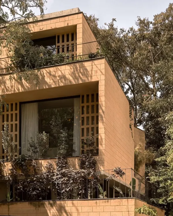 The Debris Block House in Bangalore is surrounded by trees, allowing for full-height windows and jaali screens. The stepping volumes are built with blocks made from debris from the original structure that once stood on this plot.