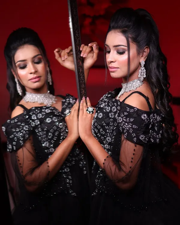A dramatic mirror shot of a model in my black off-shoulder ball gown. The smoky makeup and sparkling diamond jewelry complete this glamorous look, perfect for a grand evening event.