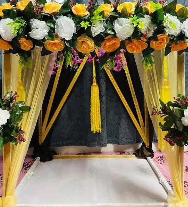 A close-up of a bright and sunny canopy decoration. This setup uses vibrant yellow and white artificial roses with yellow fabric drapes, creating a welcoming and auspicious space for Ganpati sthapana.