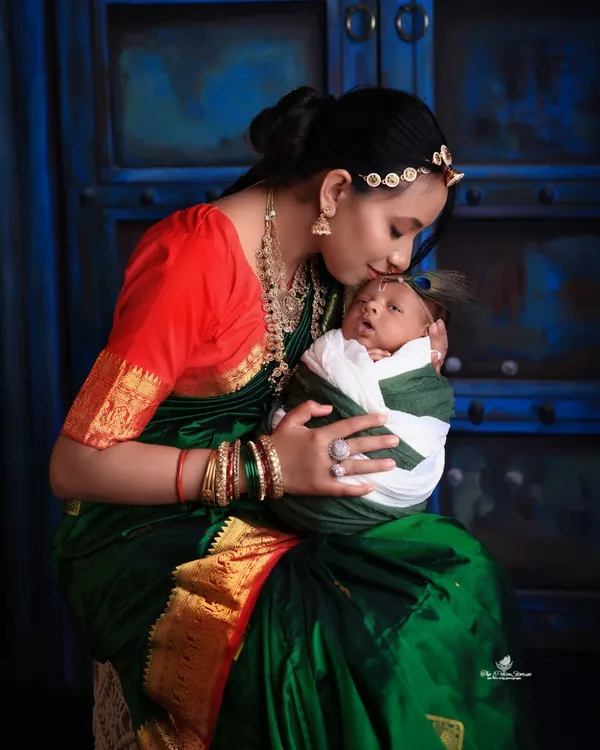 A timeless portrait capturing the tender bond between a mother and her newborn. Dressed in a beautiful traditional saree, she holds her baby close, creating a classic and emotional image against a deep blue, artistic backdrop.