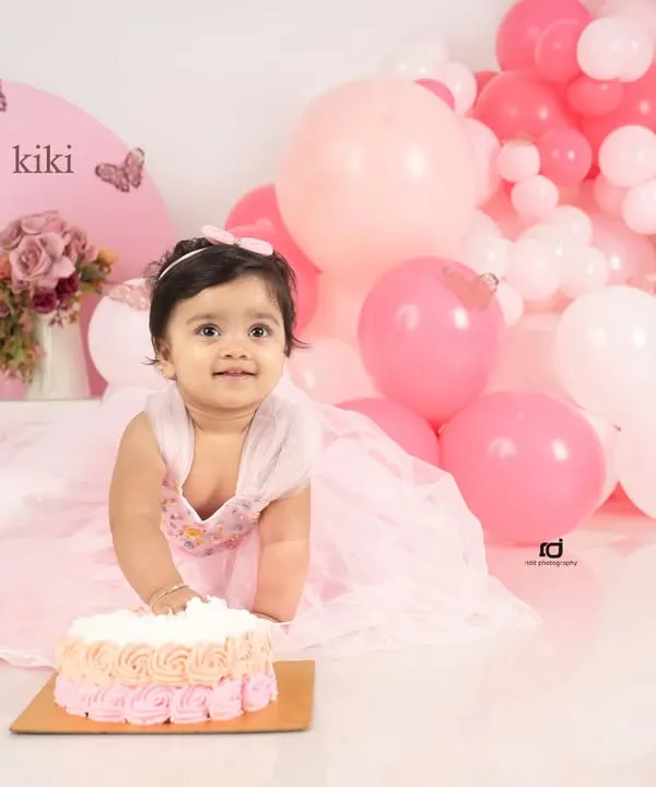 The moment of anticipation right before the cake smash begins. This little girl in her pink dress, with a butterfly-themed setup, is all smiles for her first birthday.