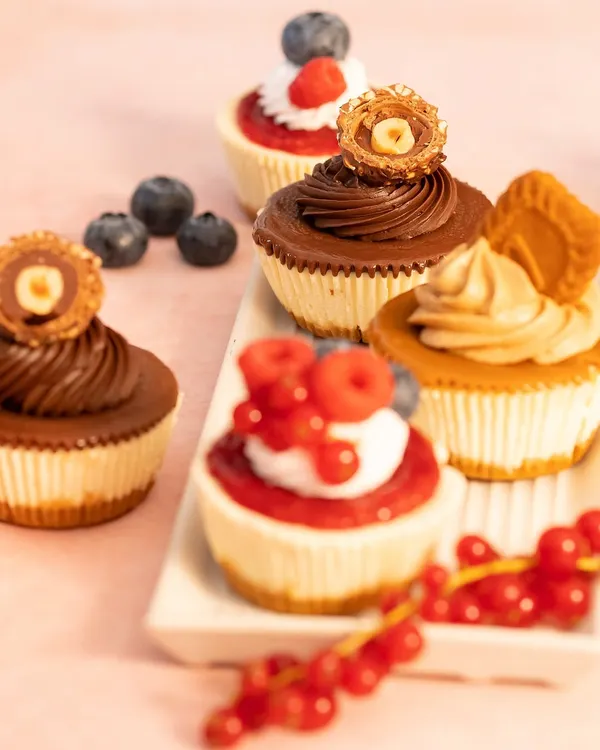 My egg-free baked baby cheesecakes are perfect for amping up your dessert table. This image shows a variety of toppings, including Nutella Rocher, Biscoff, and fresh berries.