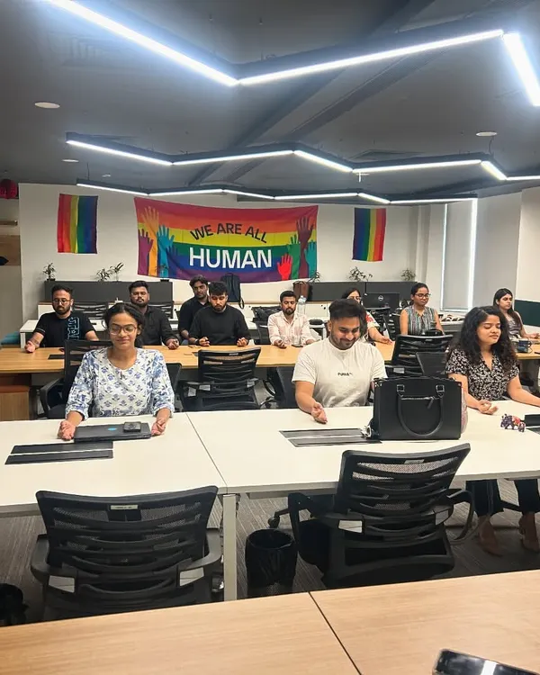 Leading a corporate yoga session at Zoo Media Network. The office is filled with a great vibe, with a "We Are All Human" pride flag in the background, reflecting a culture of inclusivity.