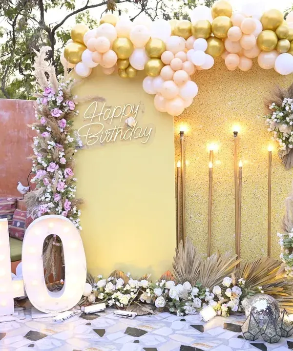 A fabulous 40th birthday celebration with a gold and glitter theme. The setup includes a shimmering backdrop, a large light-up '40', and boho-chic floral arrangements with pampas grass.