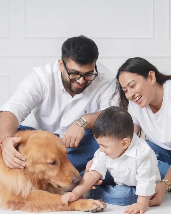 A candid family portrait capturing the pure joy and laughter between parents, their baby, and their beloved golden retriever against a clean white studio background.