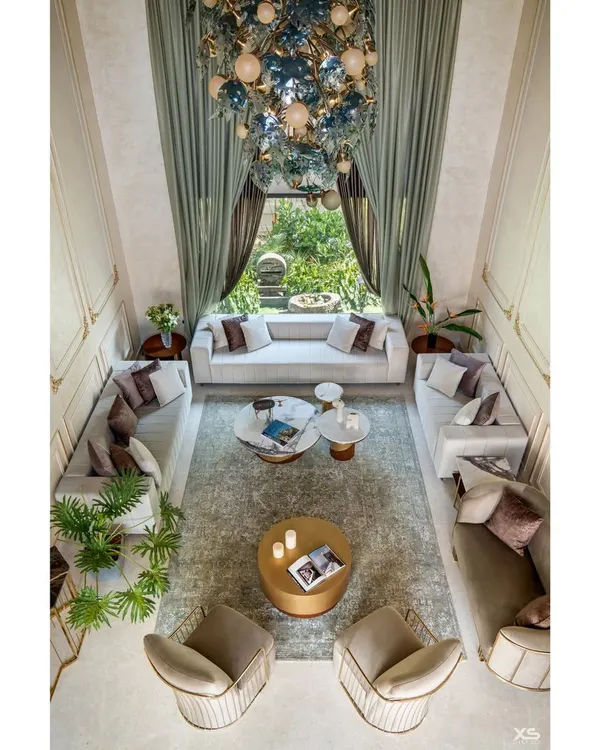 We designed this double-height living room in a luxury Bangalore villa to feel both grand and inviting. The space is organized around a stunning central chandelier, with custom furniture and expansive windows that open up to the garden, creating a seamless connection with nature.