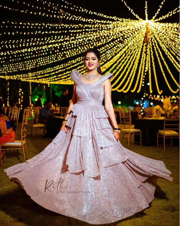 For the modern bride, a glamorous reception look. This custom-designed, shimmering rose gold gown features sculpted shoulders and a tiered, flowing skirt, perfect for a cocktail party or evening celebration.