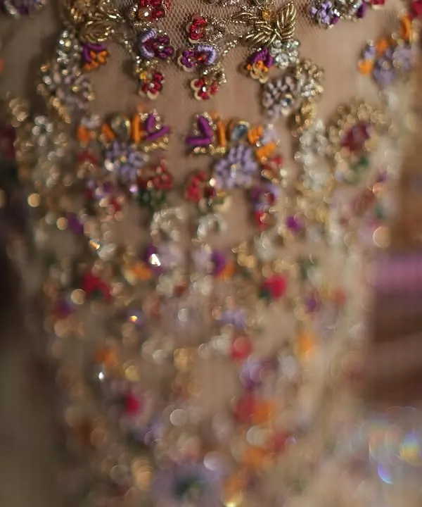 A macro shot of a bridal blouse sleeve, showing the texture and dimension of hand set Zardozi and colorful threadwork. This level of detail is what makes a custom piece truly special.