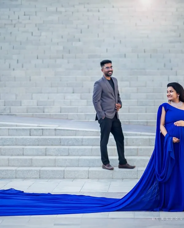 A grand, elegant portrait for the expecting couple. The flowing gown and architectural background create a sense of timeless sophistication.