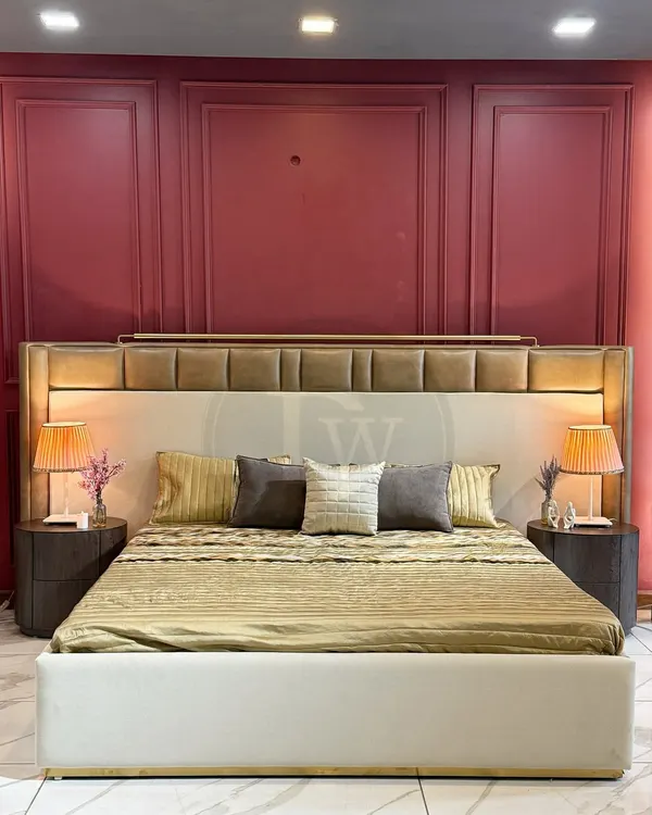 A luxury bed featuring a tall, multi-panelled headboard with integrated lighting. Paired with dark wood side tables and set against a dramatic burgundy wall, this design creates a hotel-like, opulent bedroom experience.