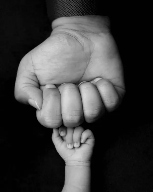 A powerful black and white image of a newborn's tiny fist held against their parent's larger one. The high contrast and simple composition make this a striking and symbolic photo.
