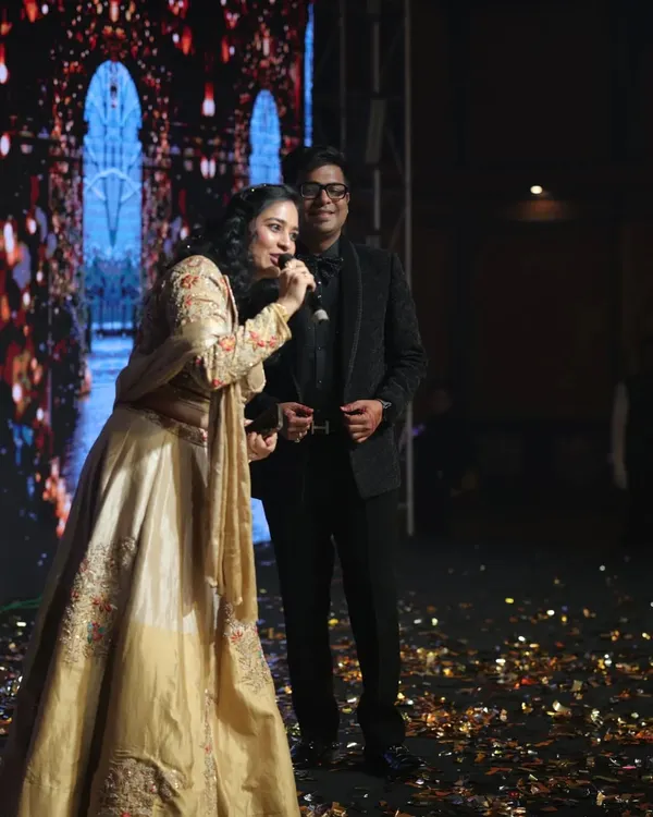 On stage during a grand Sangeet night. With a dazzling backdrop and a mic in hand, I'm ready to get the performances started and keep the energy high all night long.