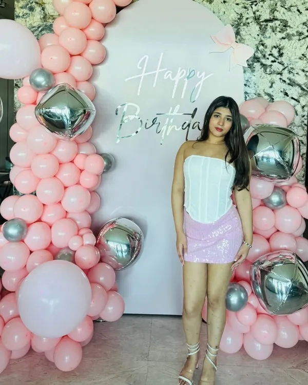Main character energy for a home birthday party. This setup features a pink backdrop with silver lettering, framed by an organic garland of pink and silver balloons for a fun and glamorous look.