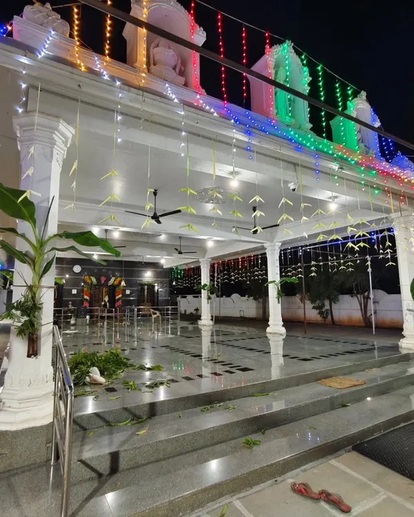 A wide view of the Vasavi Matha Temple decorated for a festival, with colorful lights, banana plantains, and hanging leaf decorations.