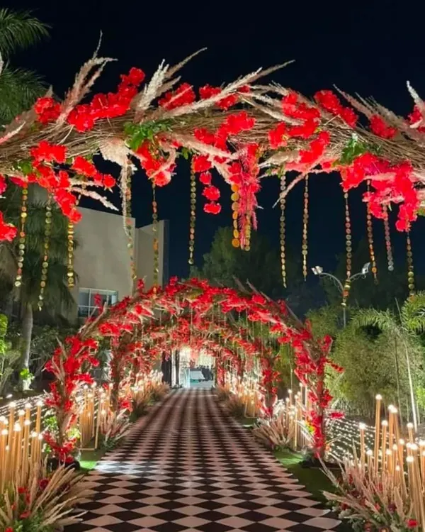 A breathtaking entrance for a cocktail night, designed with arches of bold red florals and pampas grass. The checkered walkway and warm lighting create a dramatic and luxurious welcome for your guests.