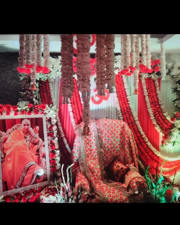 A classic red and white themed stage for a Guruji Satsang. This decoration features a draped backdrop, hanging tuberose garlands, and a floral frame for Guruji's portrait.