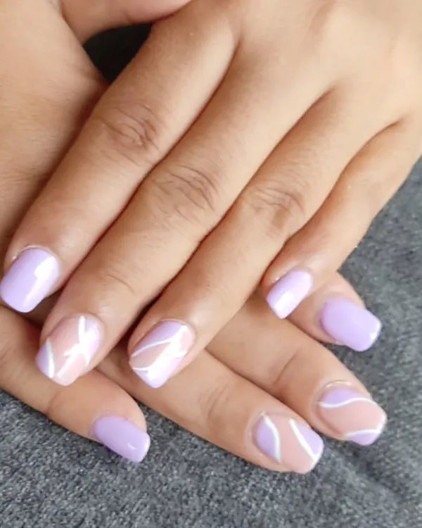 This stylish set features a mix of solid lavender nails and accent nails with abstract white swirls on a nude base. The combination is modern, soft, and artistic.