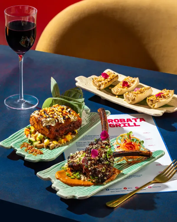 A vibrant spread of Japanese robata grill items, including lamb chops and paneer skewers, styled with a glass of red wine for a modern dining experience.