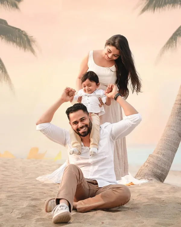 A classic family portrait on the beach, with a beautiful sunset sky. The father holds his son on his shoulders, creating a joyful and timeless image of family love.