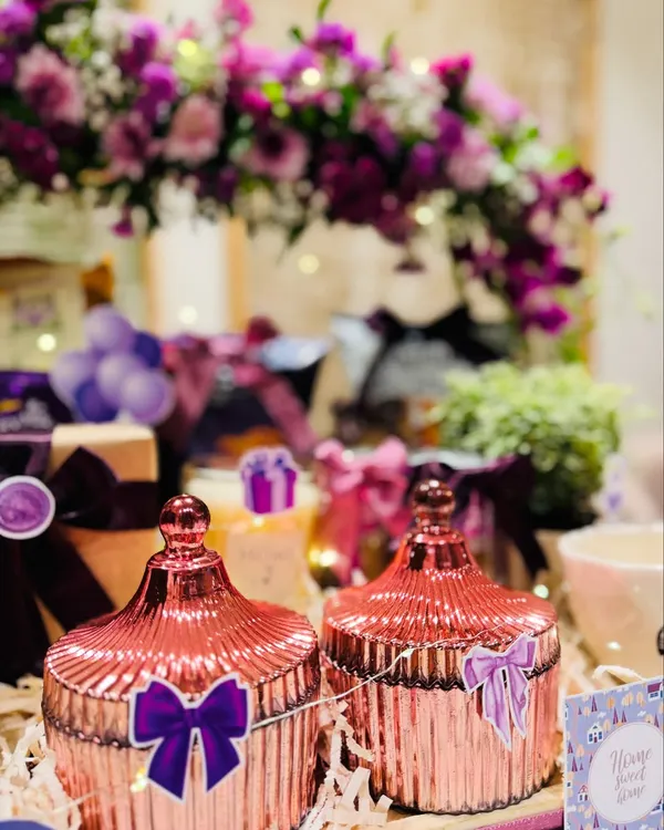 A close-up of the decorative elements in our 'Home in Hues' hamper. The shimmering rose-gold jars and fresh purple flowers add a touch of magic and elegance to a new living space.