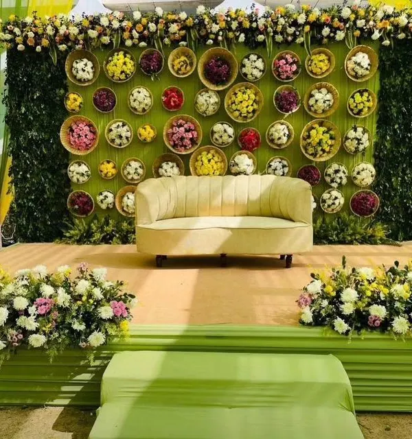 A beautiful Mehendi stage with a backdrop of a green wall decorated with baskets of colorful flowers. This creates a fresh, garden-like feel for photos.