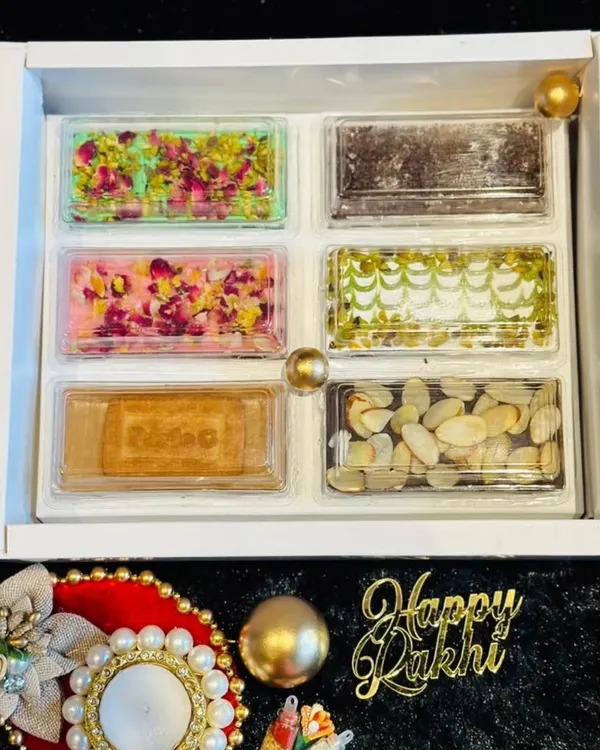 This elegant white Rakhi hamper contains six different varieties of my fusion chocolate bars. Flavors include rose petal, pistachio, Oreo crumble, and nutty delights, offering a taste for every palate.