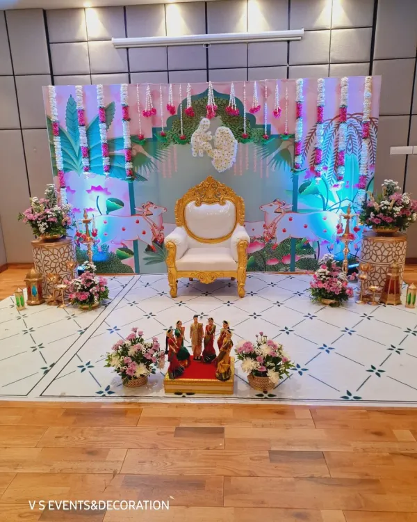 A wide view of a Sreemantham setup, showing the main seating area, floral arrangements on pedestals, and decorative props. The printed backdrop with lotus and cow motifs adds a gentle, traditional feel to the modern layout.