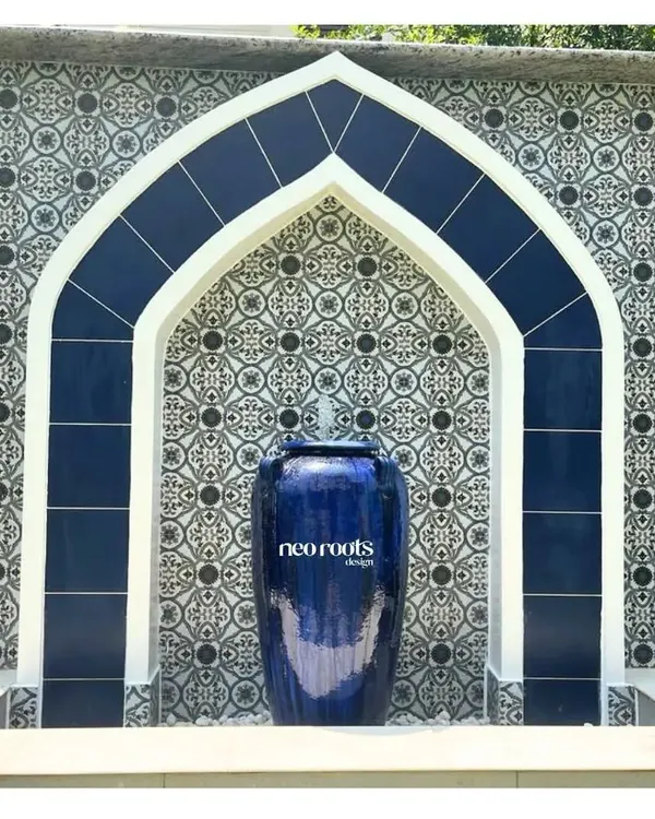 A close-up of a magnificent Moroccan-style water feature. The deep blue ceramic urn and matching arched tilework create a striking visual, while the gentle flow of water adds a calming auditory element to the garden.