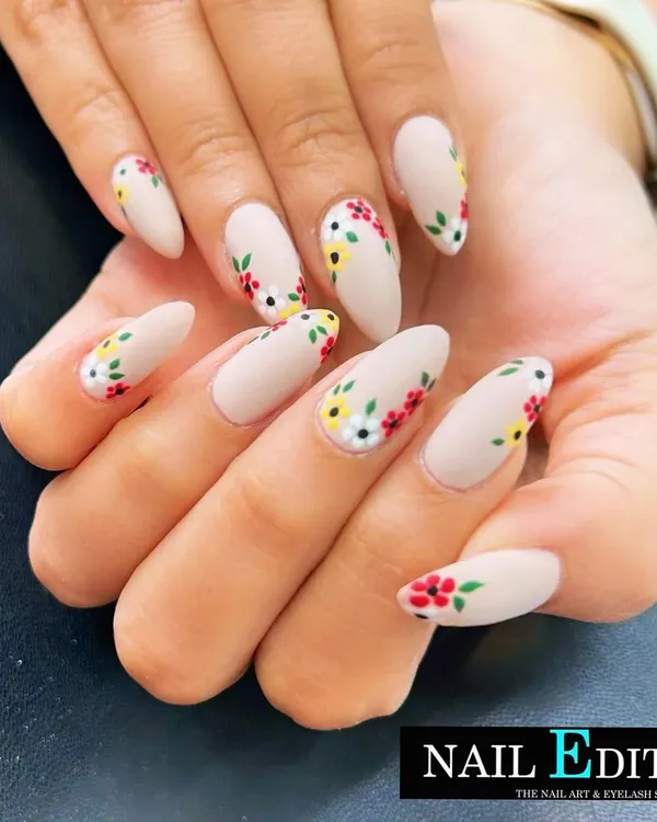 A beautiful and delicate floral design on a matte nude base. The tiny, hand-painted flowers in red, yellow, and white are placed artfully along the sides of the almond-shaped nails for a fresh, garden-inspired look.