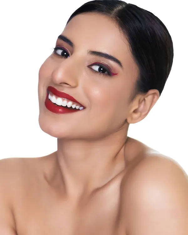 A clean, bright headshot perfect for an actor's portfolio. The focus is on the model's warm smile and the striking red winged eyeliner, showing off personality and makeup artistry.
