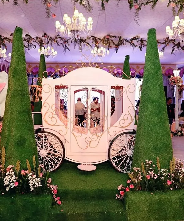 A picture-perfect entrance for a modern fairytale. We designed this custom-built carriage as a magical photo opportunity, framed by sculpted topiaries and delicate pink flowers to set a whimsical tone for the entire event.