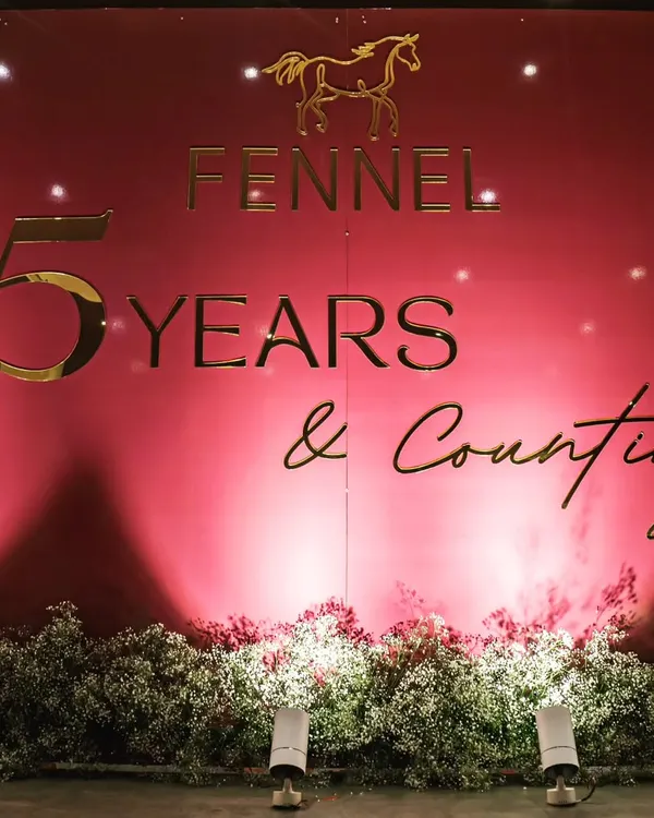 A chic and impactful backdrop for the 15th-anniversary celebration of fashion brand Fennel. The design uses a bold color, gold lettering, and a bed of baby's breath for an elegant look.