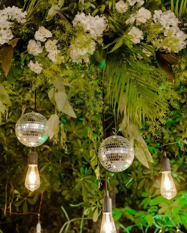 A close-up of our lighting and floral design for an evening event. We combined rustic Edison bulbs with mini disco balls and lush greenery to create a unique and magical ambiance.